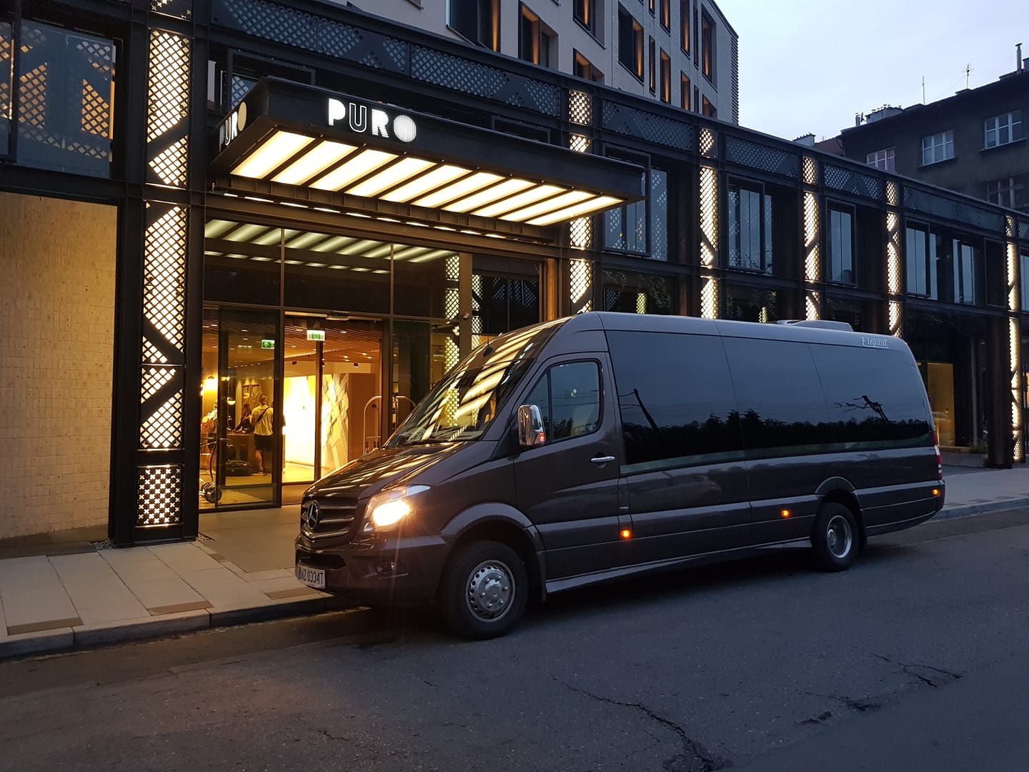 Ciemny Mercedes Sprinter z floty Trans-Prestige zaparkowany przed hotelem o zmierzchu — wynajem autobusu lub busa w Warszawie